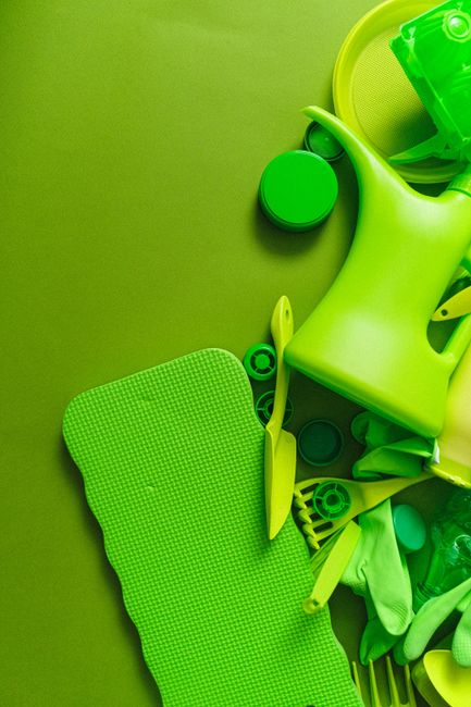 A collection of green household items, including plastic storage containers, a chair, and various packaging materials, are scattered on a green surface. Some items appear to be partially wrapped or pl