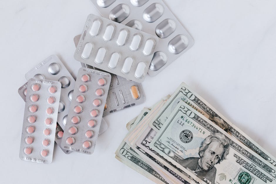 A collection of blister packs containing pink and white pills, some with rounded or oblong shapes, are scattered on a white surface next to a stack of US twenty-dollar bills. The pills are arranged with some still in their transparent plastic and foil packaging, while others have been removed from the blister packs. The money is partially visible, with the bills fanned out, showcasing the $20 denomination with Andrew Jackson's portrait. The scene captures the items in a flat-lay style, with a focus on the medication and cash, possibly indicating an aspect of healthcare, pharmaceuticals, or financial transactions related to moves or relocations. The environment appears clean and well-lit, with no background details, emphasizing the objects themselves. The image exemplifies packing and logistics in a house removal context, subtly referencing moving preparation or expenses involved, aligning with the services of [COMPANY_NAME] and the topic of relocation costs in Haringey.